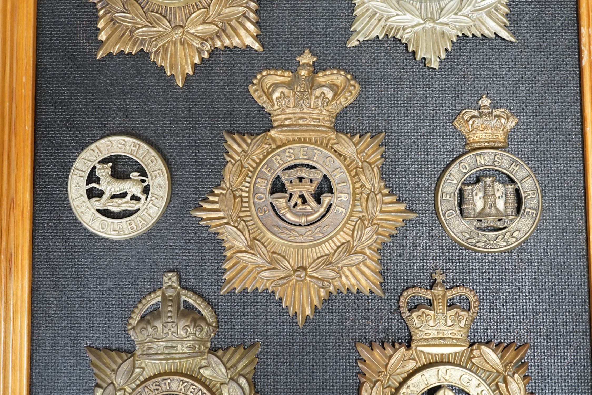 Five military helmet plates and two other centre badges, mounted on a board including; the Essex Regiment, the North Staffordshire 1st Volunteer Battalion, the Somerset Regiment, the Buffs East Kent Regiment, the King’s